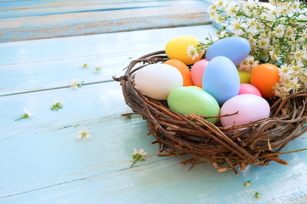 Kleurrijke paaseieren in nest met bloemen op blauwe houten achtergrond