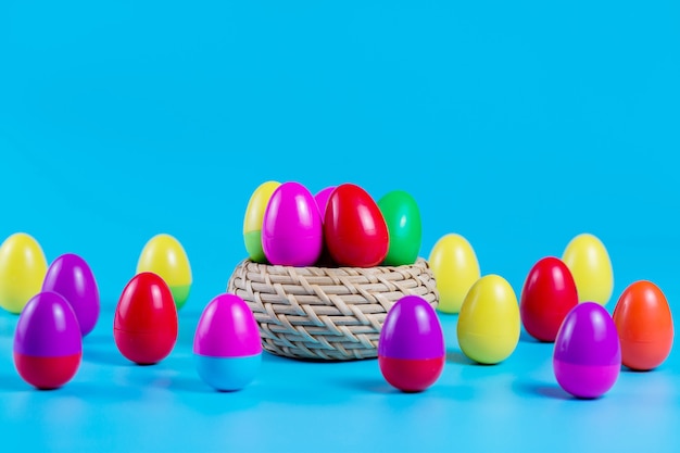 Kleurrijke plastic easter eggs in een rieten mand op blauwe achtergrond.