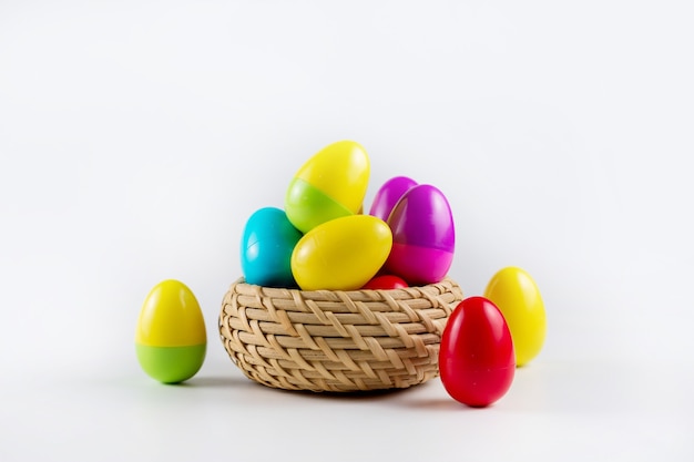 Kleurrijke Plastic Easter Eggs in een rieten mand op witte achtergrond.