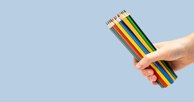 Kleurrijke potloden gekleurde benodigdheden voor kunst in de hand op blauwe promoachtergrond van de advertentiebanner