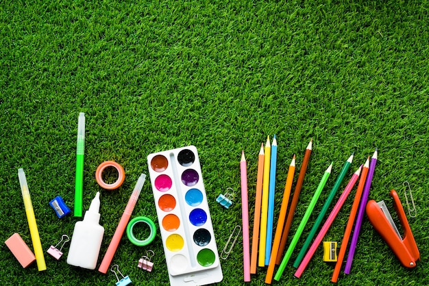 Kleurrijke potloden, verf, schoolbenodigdheden en plasticine op groen gras, bovenaanzicht