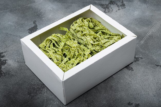 Kleurrijke rauwe Italiaanse tagliatelle pasta in box set, op grijze stenen tafel achtergrond