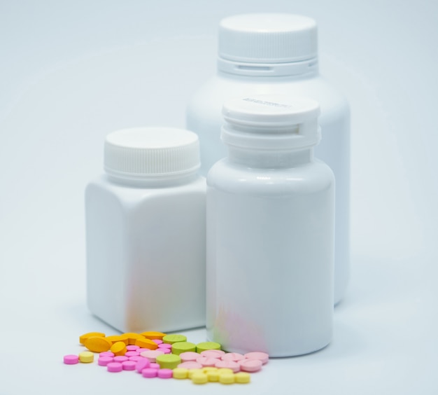 Kleurrijke tabletpillen met gesloten witte flessen op witte achtergrond met leeg etiket. Farmaceutische industrie. Geneesmiddelinteractie. Apotheek achtergrond. Farmaceutische producten. Pasteltabletten pillen.