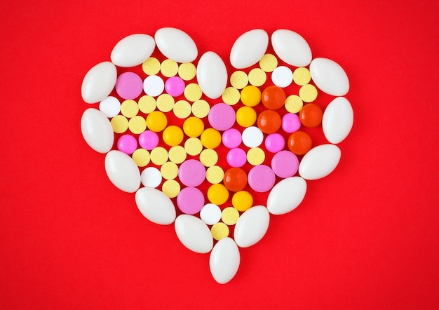 Foto kleurrijke tabletten gerangschikt in de vorm van een hart op rode achtergrond. symbool foto van hart-en vaatziekten, medicatie en geneesmiddelen. medicijnpillen of capsules hartvormig op rode achtergrond