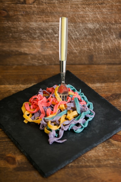 Foto kleurrijke tagliatelle met vork op zwarte plaat, houten scèneclose-up, culinair concept