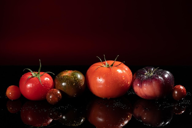 Kleurrijke tomaten van verschillende maten en soorten op rode donkere achtergrond met kopieerruimte