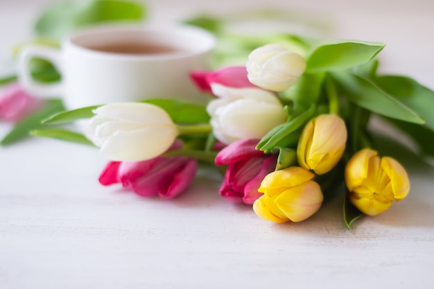 Kleurrijke tulpen en kopje thee op de witte houten tafel