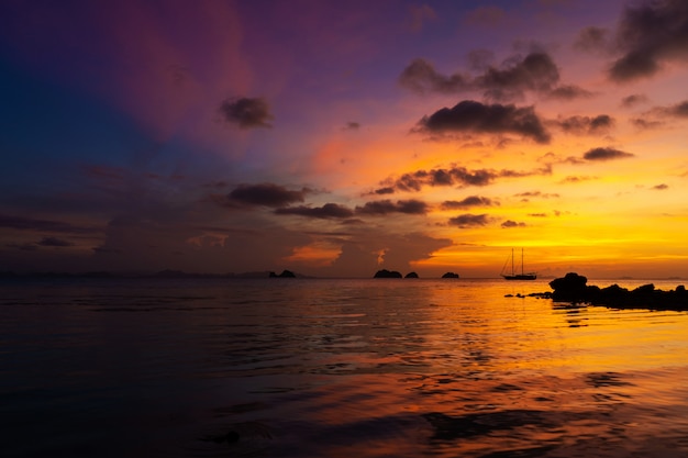 Kleurrijke zonsondergang op een tropisch strand. Oranje zonsondergang op de Oceaan. Kleurrijke zonsondergang in de tropen. In het water ligt een zeilschip. Silhouet zeilboot met masten