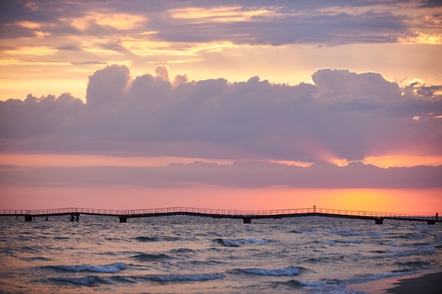 Kleurrijke zonsopgang boven de zee. Pier aan de horizon.