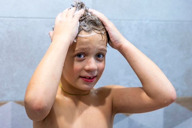 Kleuterjongen wast zijn hoofd met zijn handen in de badkamer met shampoo