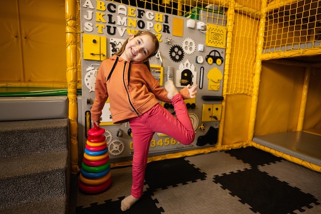 kleutermeisje speelt met een gekleurde piramide in handen tegen een druk bord in het kinderspeelcentrum