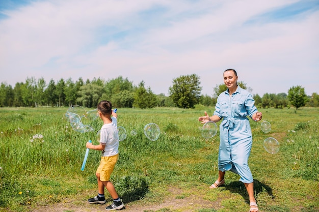 Kleuters van moeder en zoon brengen in de zomer tijd buiten door en blazen grote zeepbellen