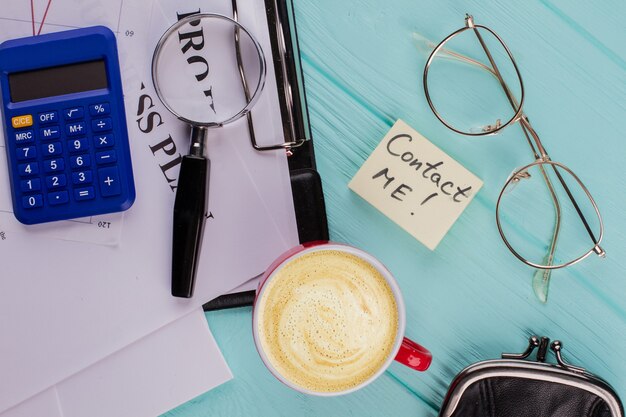 Kleverig papier met contact met mij woord op kantoor tafel. Kopje koffie papieren glazen vergrootglas opleggen van blauw bureau.