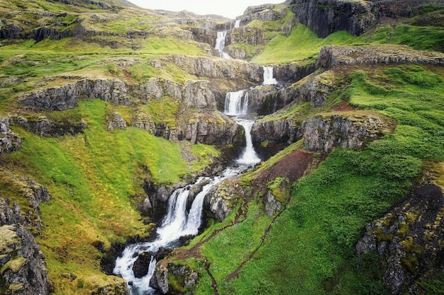 Klifbrekkufossar waterval met zeven niveaus stroomt verborgen in de Mjoifjordur Fjord in de zomer in IJsland