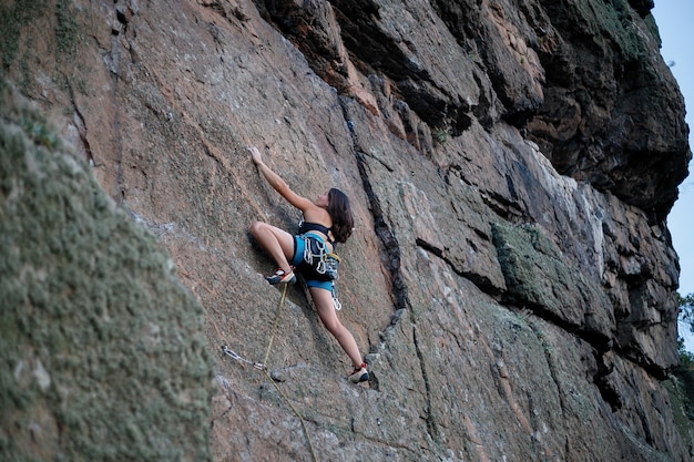 Klimmer overwint uitdagende klimroute. Een meisje beklimt een rots. Vrouw die zich bezighouden met extreme sporten. Extreme hobby. uitzicht vanuit de verte, een meisje klimt met een lager touw