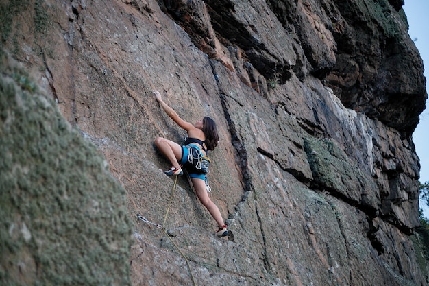 Klimmer overwint uitdagende klimroute. een meisje beklimt een rots. vrouw die zich bezighouden met extreme sporten. extreme hobby. uitzicht vanuit de verte, een meisje klimt met een lager touw