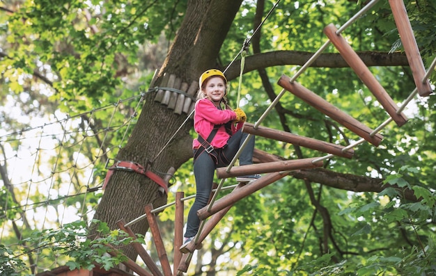 Klimmerkind bij het trainen van een gelukkig kind dat belt terwijl hij in de hoge boom en touwen klimt