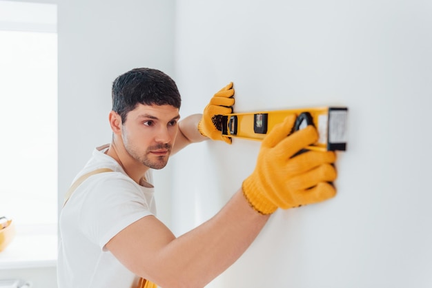 Klusjesman in geel uniform controleert niveaus van muur Huisrenovatieconcept