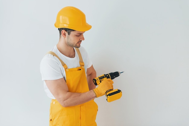 Klusjesman in geel uniform staande tegen witte muur met automatische schroevendraaier Huisrenovatieconcept