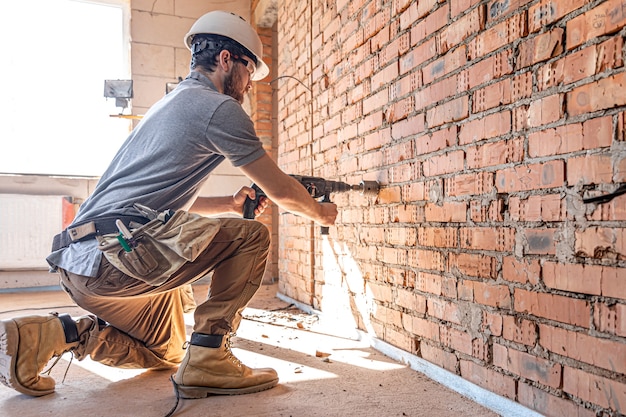 Klusjesman op een bouwplaats tijdens het boren van een muur met een perforator.