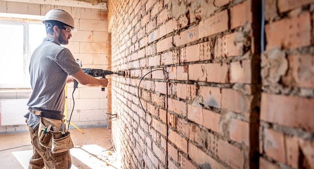 Klusjesman op een bouwplaats tijdens het boren van een muur met een perforator