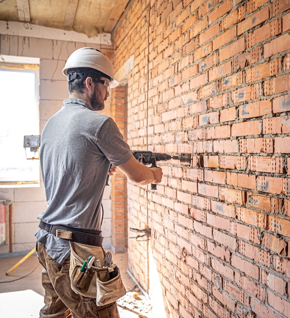 Klusjesman op een bouwplaats tijdens het boren van een muur met een perforator.