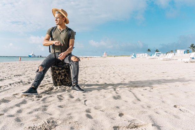 Knap en fit man poseren met een kleine koffer Een man op het strand overweegt de oceaan