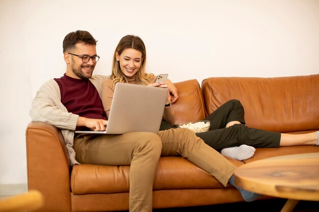 Knap jong stel dat samen laptop gebruikt terwijl ze thuis op de bank zitten