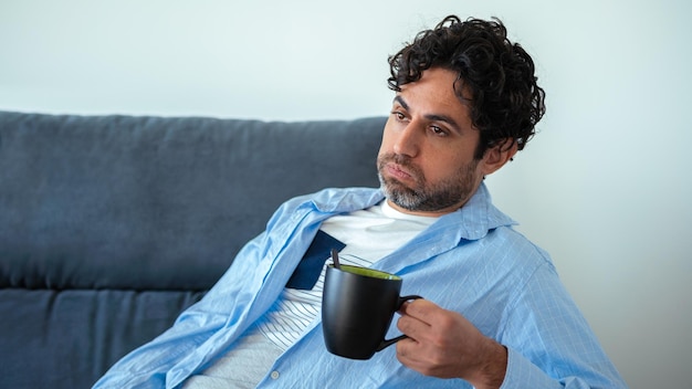 Knap mannelijk model voelt zich moe na het werk en het hebben van een café. volwassen man die 's ochtends espressokoffie drinkt terwijl hij hoofdpijn heeft terwijl hij op de bank thuis zit. onaangename pijn.