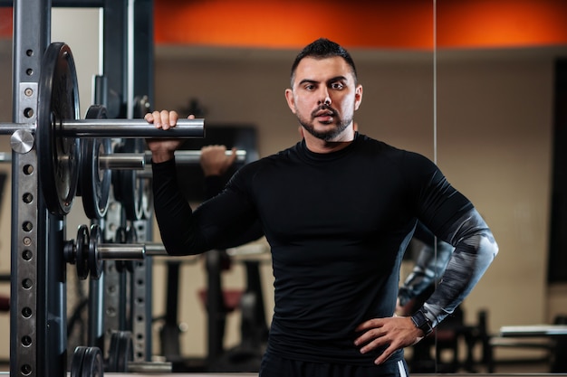 Knap met grote spieren die naast de barbell poseren