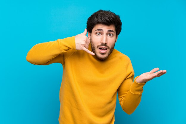 Knap over geïsoleerde blauwe muur telefoon gebaar maken en twijfelen