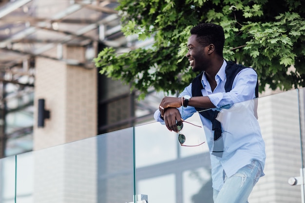 Knappe afrikaanse man die naar de camera kijkt in de straat van de zomerstad. Poseren.