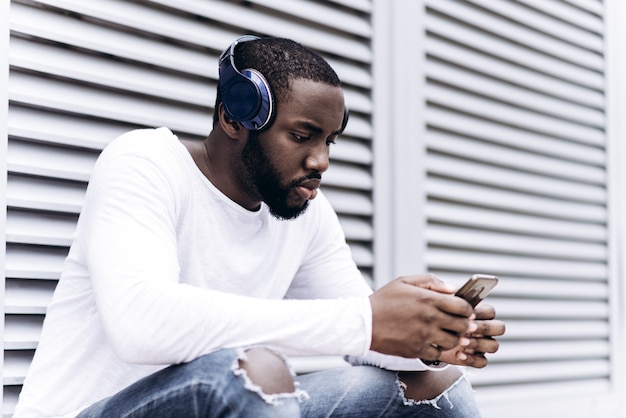 Knappe Afro-Amerikaanse man die casual kleding draagt ​​in moderne stad luisteren naar muziek met koptelefoon