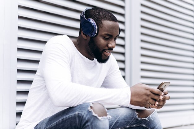 Knappe Afro-Amerikaanse man die casual kleding draagt ​​in moderne stad luisteren naar muziek met koptelefoon