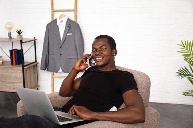 Knappe Afro-Amerikaanse man met laptop die thuis telefonisch praat