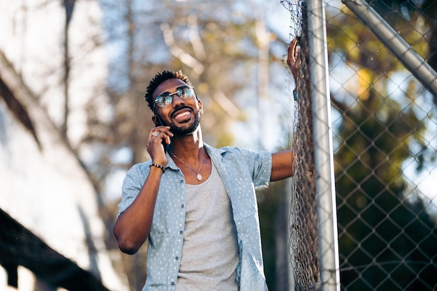Knappe Afro-Amerikaanse man met zijn smartphone op straat glimlachend
