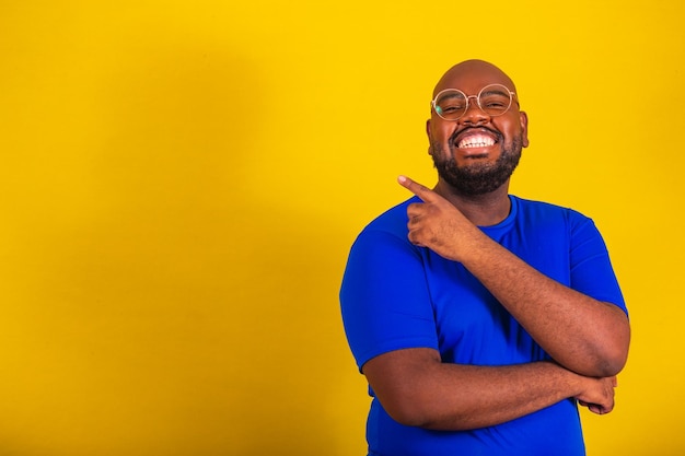Knappe Afro-Braziliaanse man met een bril blauw shirt over gele achtergrond met handen en vingers wijzend naar de zijkant reclame reclame kopie ruimte negatieve ruimte
