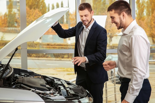 Knappe autoverkoper met stagiair die naar de motor van de auto kijkt in het dealercentrum