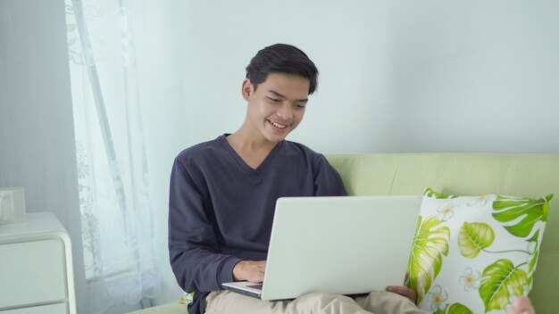 Knappe aziatische man die thuis geniet van het kijken naar zijn laptopscherm