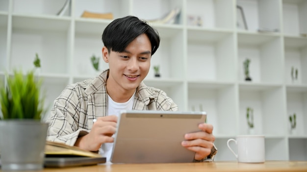 Knappe Aziatische man in causale outfit met behulp van digitale tablet-touchpad aan zijn bureau in kantoorruimte