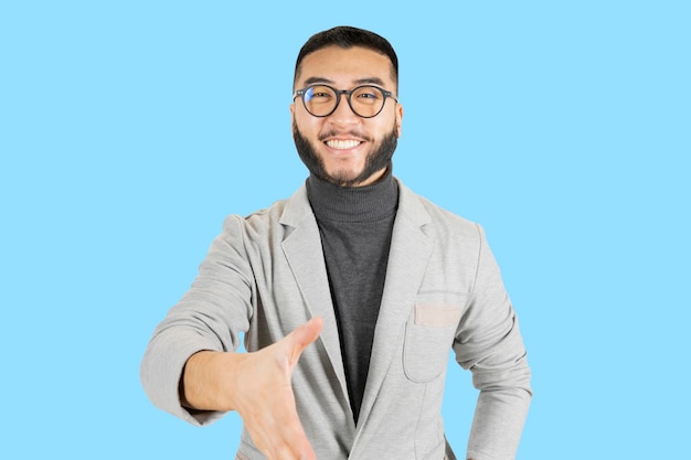 Knappe aziatische man met bril en baard in een jasje van zakenman39s handen schudden met een zelfverzekerd gebaar blauwe achtergrond