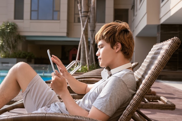 Knappe Aziatische man ontspannen bij het zwembad en het lezen van e-book