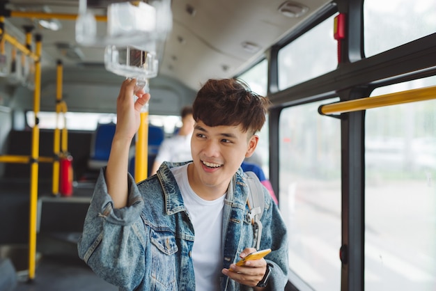 Knappe aziatische man zit in de stadsbus en typt een bericht aan de telefoon.