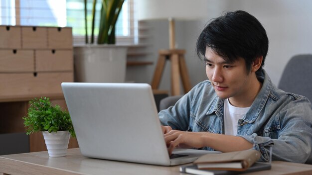 Knappe aziatische man zit in de woonkamer en surft op internet met een computerlaptop