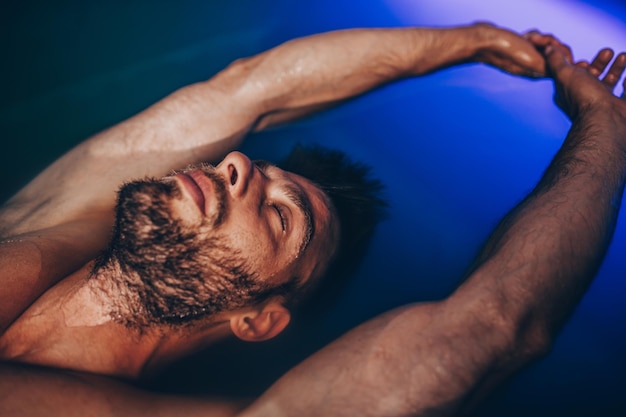 Foto knappe baardman drijvend in tank gevuld met dicht zout water dat wordt gebruikt in meditatie, therapie en alternatieve geneeskunde.