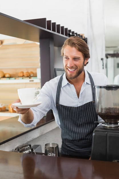 Knappe barista die een kop van koffie aanbiedt