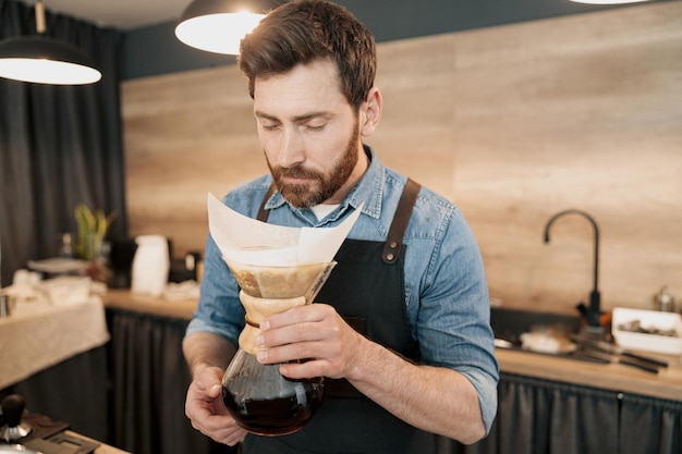 Knappe barista met stijlvolle baard ruikende filterkoffie in cafetaria