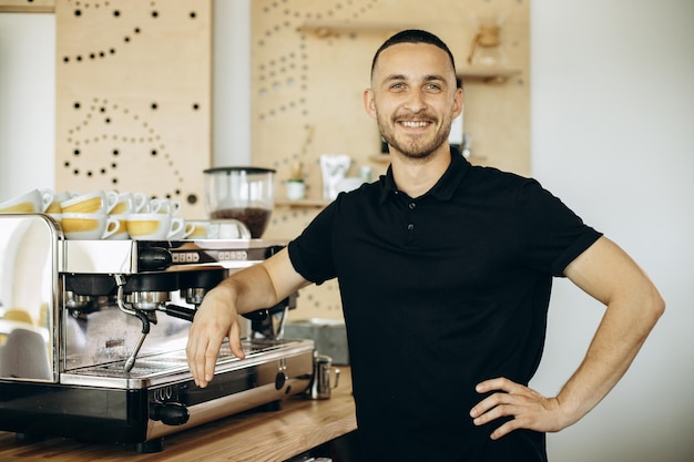 Knappe barista staat bij de koffiemachine in de coffeeshop