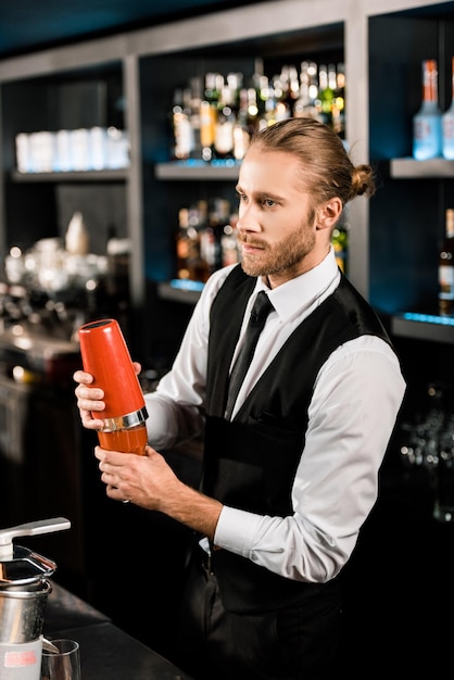 Foto knappe barman die cocktail in shaker mengt