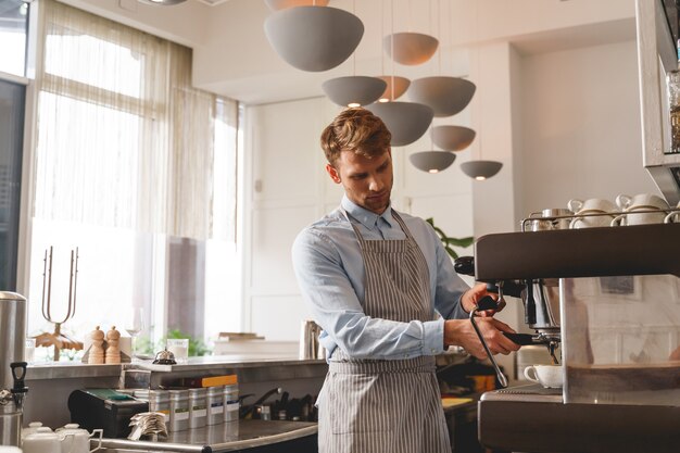 Knappe barman in schort die warme drank uit de kraan van de koffiemachine in de beker giet